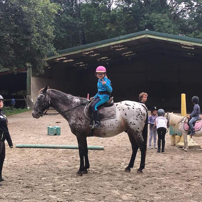 Une fille fait le signe de la victoire à dos de cheval lors d'une colonie de vacances bretagne