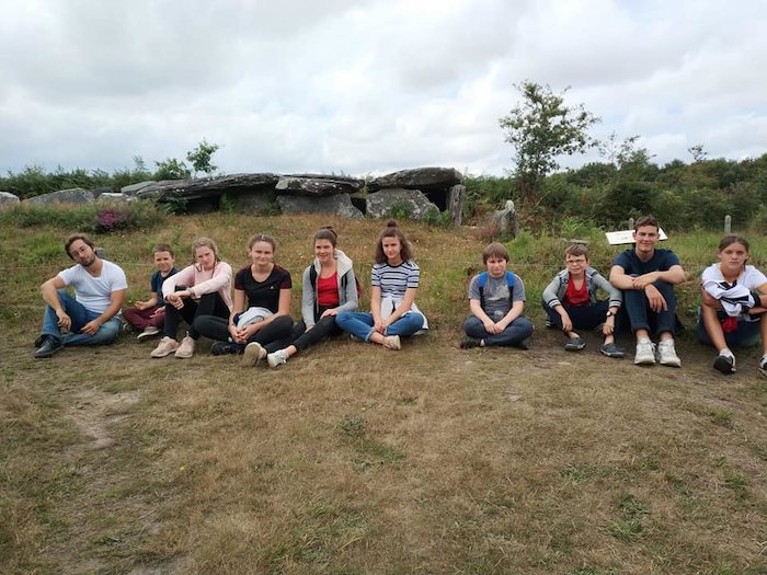 Les ado sont assis et alignés dans l'herbe après la randonnée lors d'une colonie de vacances Bretagne