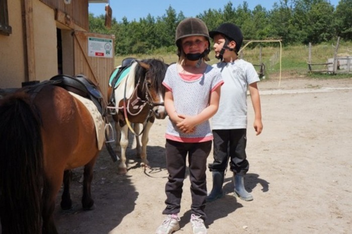 Des enfants avec les poneys pendant une colonie de vacances équitation