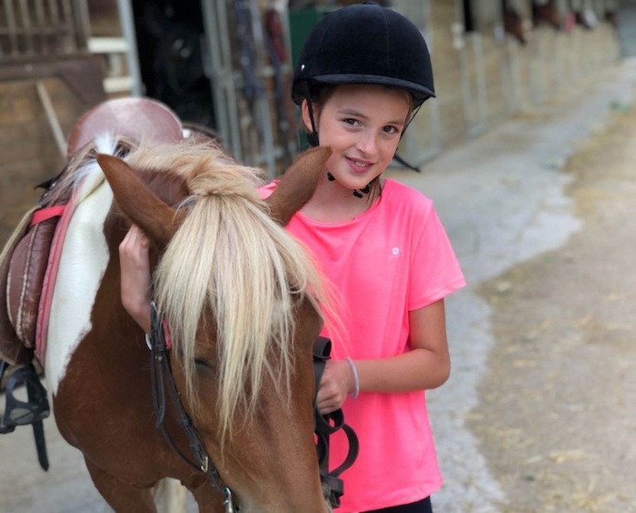 Jeune fille en rose sourit avec poney en camp de vacances été