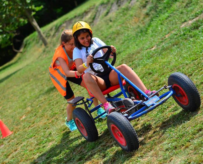 Jeune fille pousse une autre fille en kart à pédales lors d'une colonie multisport
