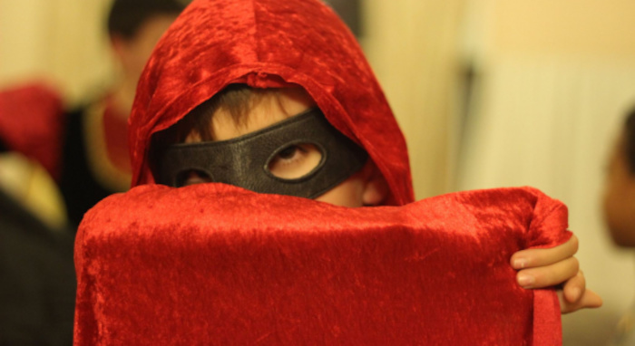 Garçon portant une cape rouge et un masque noir lors d'une colonie de vacances artistique