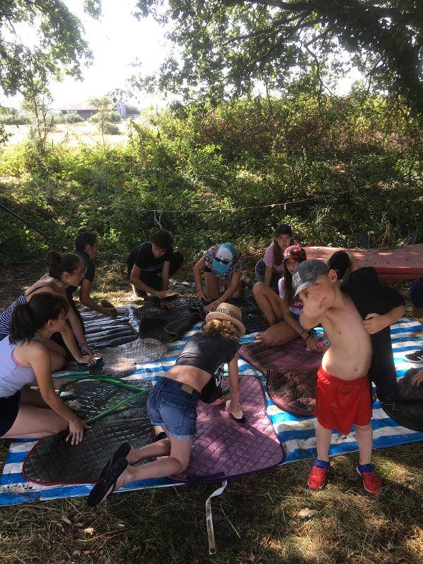 Les enfants nettoient leur matériel d'équitation sur une bâche en plein air lors d'une colonie de vacances d'équitation en gironde