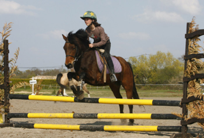 Une fille saute un obstacle avec un cheval lors d'une colonie de vacances d'équitation.