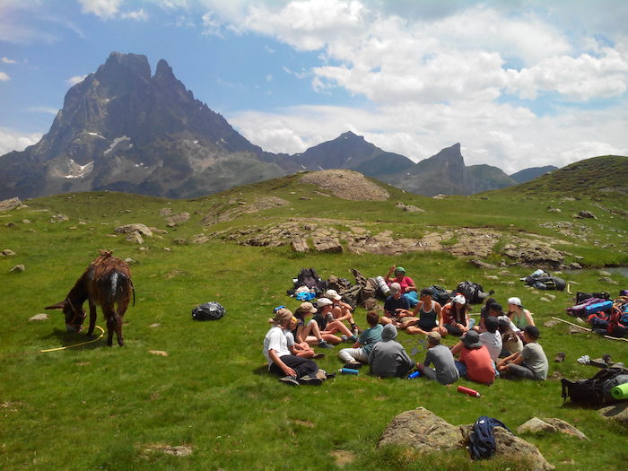 les participants sont assis dans l'herbe au sommet de la montagne  lors d'une colonie de vacance nature dans les Pyrénées
