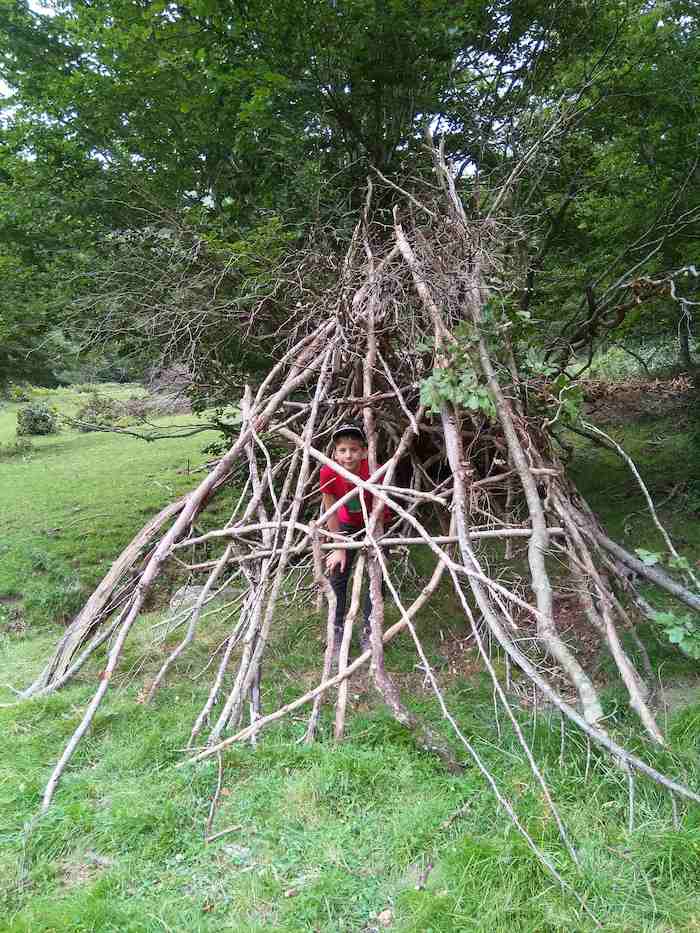 Un enfant se trouve dans une cabane faite de branches lors d'une colonie de vacance nature dans les Pyrénées