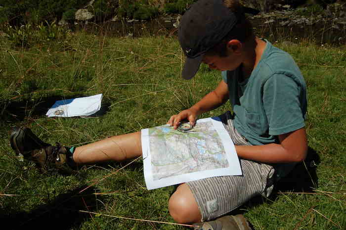Un enfant se repère à l'aide d'une boussole et d'une carte  lors d'une colonie de vacances dans les Pyrénées.