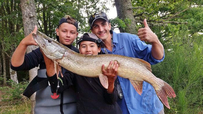 Deux garçons et un animateur posent avec un poisson fraîchement pêché