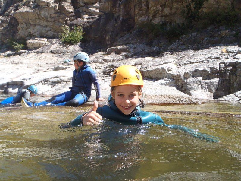 enfant qui lève le pouce dans la rivière avec une combinaison