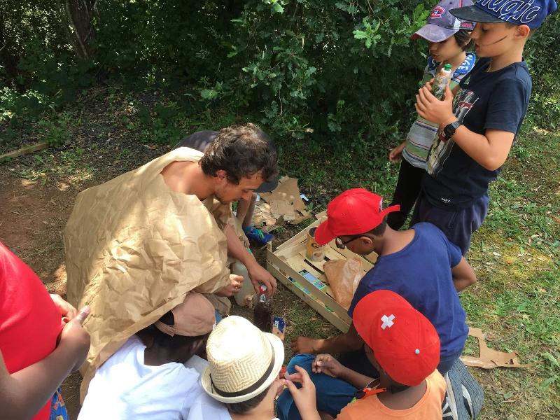 Un moniteur montre aux enfants comment filter de l'eau dans le jardin lors de leur colonie de vacances survie
