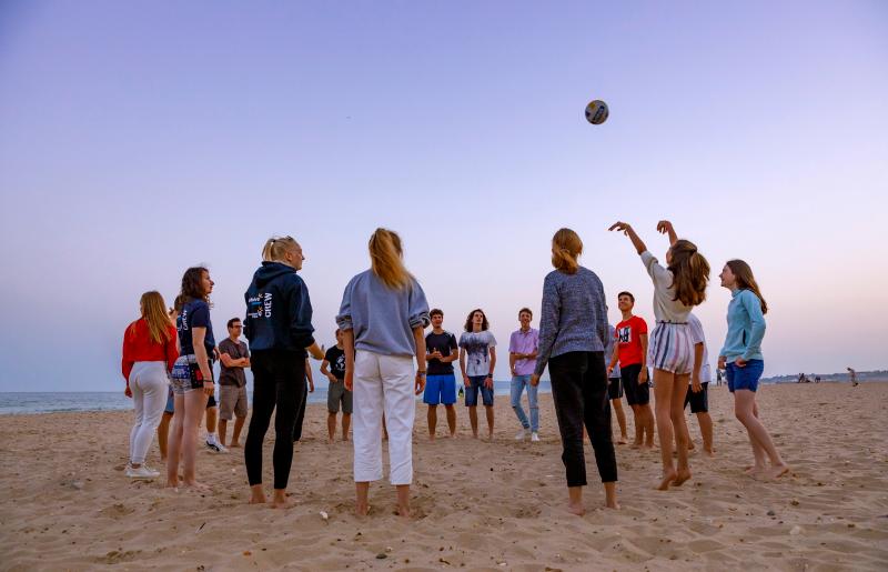 Des jeunes en cercle font du sport avec un ballon sur la plage