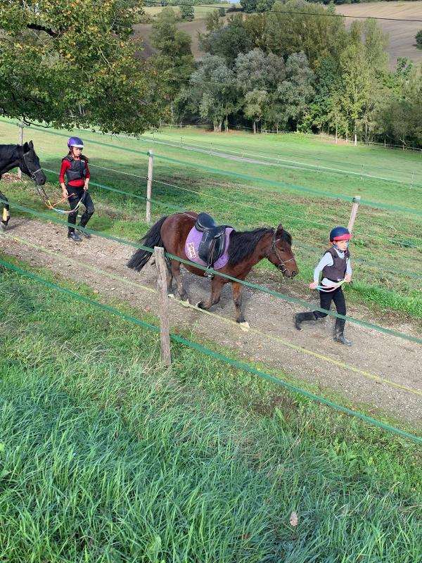 Deux enfants mènent leur cheval à la longe sur un sentier en colonie de vacances équitation
