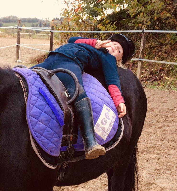 Une fillette est allongée sur la croupe de son cheval en colonie de vacances équitation
