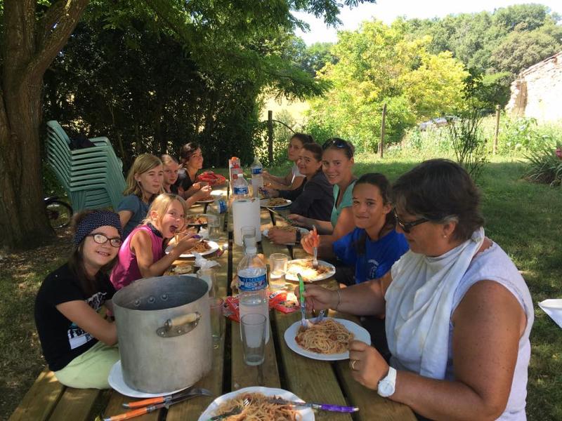 Les enfants et animateurs de la colonie de vacances équitation mangent des spaghettis sur une table en extérieur lors de la colonie de vacances équitation