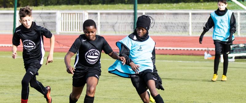 trois jeunes courent et jouent au ballon sur un terrain de football en colonie de vacances sportif