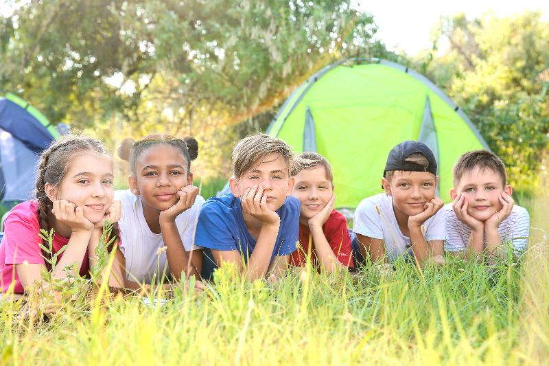 enfants couchés dans l'herbe qui regarde la caméra dans l'herbe avec des tentes derrière après une réservation anticipée