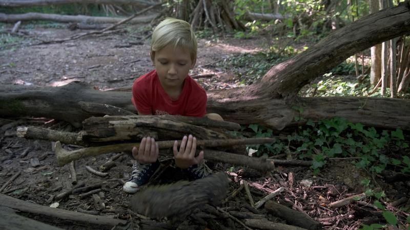 enfant qui porte du bois pour construire une cabane dans les bois en colo