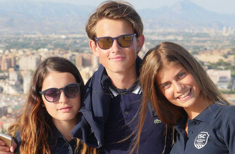 un garçon avec des lunettes de soleil et deux filles qui sourient au soleil avec une vue panoramique derrière