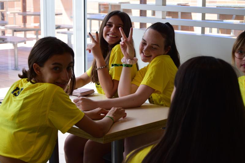 Deux filles qui font un signe de la main en souriant avec des t-shirts jaunes en séjour linguistique Espagne ado