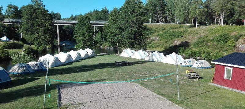 Vue sur le terrain de la colo aventure en Suède où sont plantées les tentes, avec un terrain de beach volley au milieu de l'herbe
