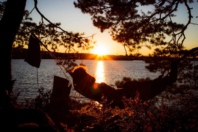 Personne couchée dans un hamac et coucher de soleil sur le lac en arrière plan lors du camp itinérant en Suède