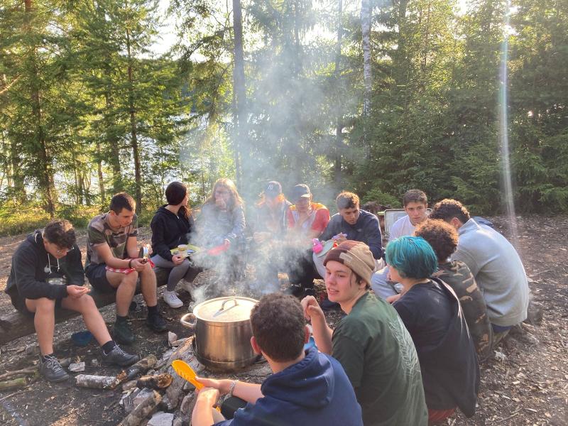 Jeunes assis en cercle dans la forêt autour d'une marmite chauffant au feu de bois pendant le camp itinérant en Suède 