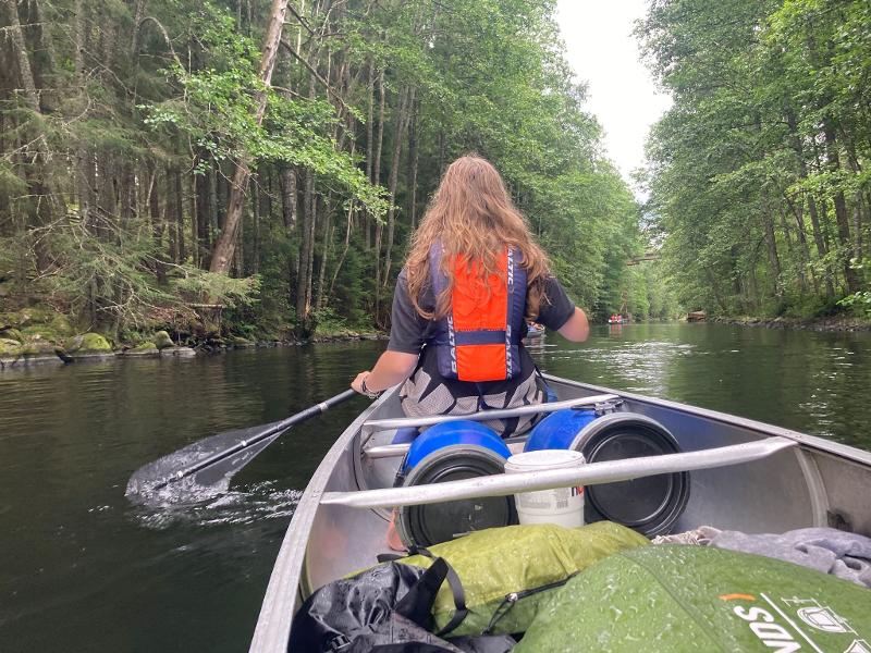 Jeune fille qui pagaie de dos, au milieu de la rivière, entre les arbres de la forêt pendant le camp itinérant en Suède