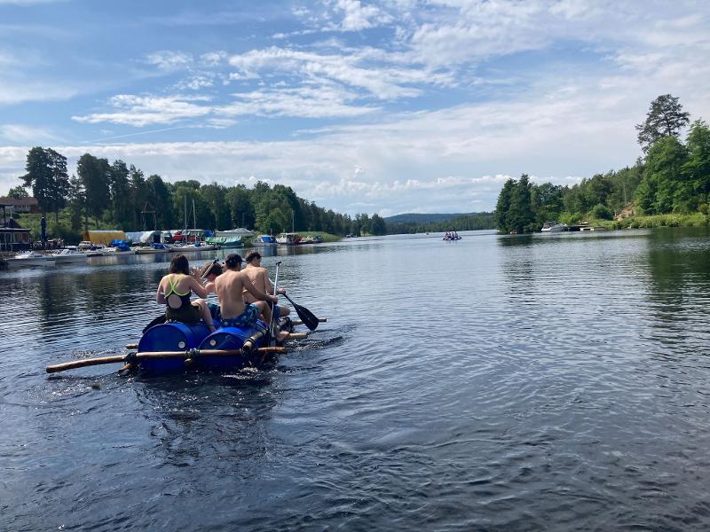 Groupe de jeunes pagayant et s'éloignant sur leur radeau de fortune fabriqué pendant la colo aventure en Suède