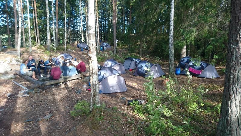 Des jeunes d'une colonie de vacances itinérante en Suède en cercle autour d'un feu dans la forêt avec leur tentes 
