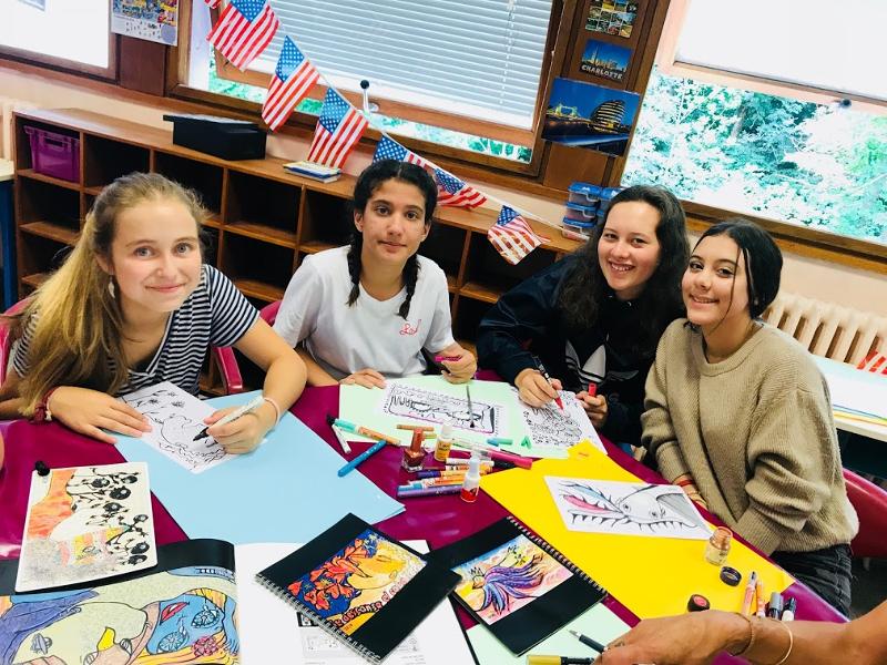 jeunes filles assises à une table qui font des activités manuelles lors d'une colo