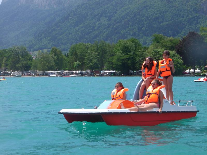 quatre jeunes dans un petit bateau sur un magnifique lac bleu turquoise avec des montagnes en fond pendant une colo