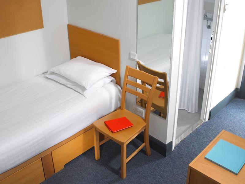 Chambre individuelle avec un lit, une chaise, un miroir et l'entrée de la salle de bain dans la résidence Maynooth lors du séjour linguistique irlande