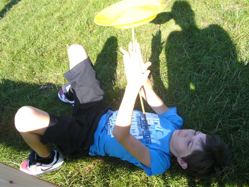 jeune garçon couché au sol dans l'herbe qui fait pivoter une assiette en plastique