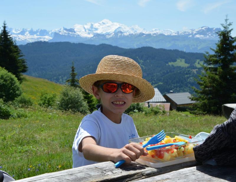 enfant à la montagne qui mange des fruits lors d'une colo sous le soleil