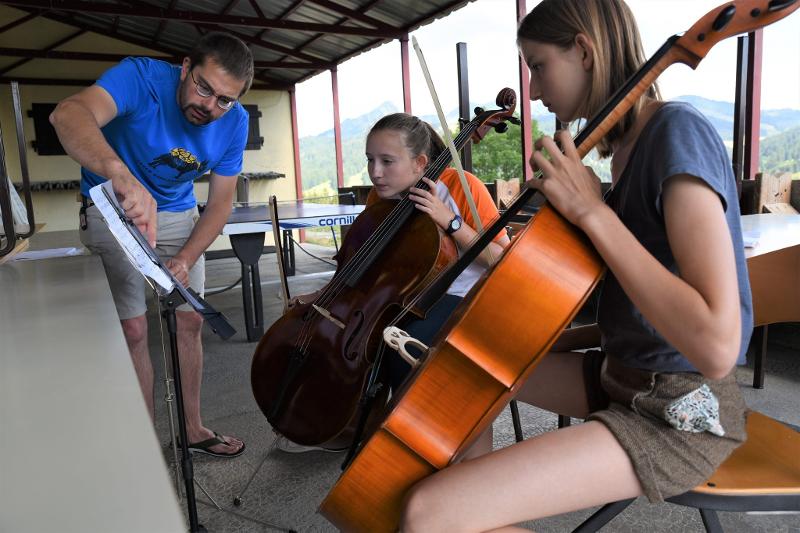 deux filles qui regardent une partition pour jouer du violoncelle en colo avec leur enseignant