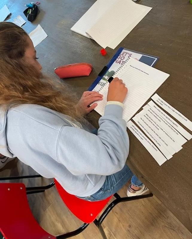 une jeune fille assise qui écrit sur des feuilles et étudie