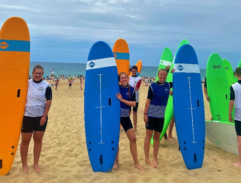 des jeunes debouts avec leurs planches de surf sur la plage 
