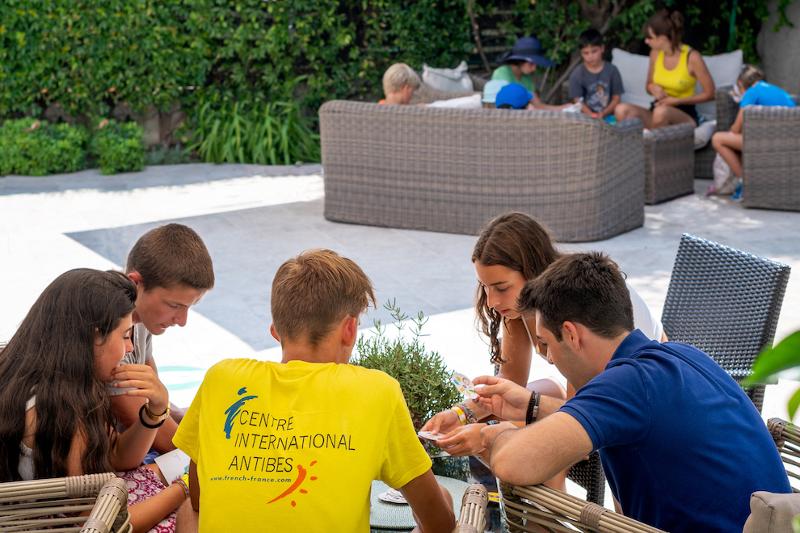 jeunes se relaxant en jouant à un jeu de carte avec un moniteur sur les salons de jardin du séjour linguistique 