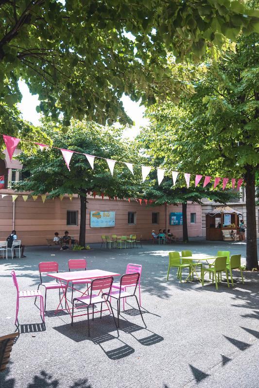 Cours extérieur du bâtiment du séjour linguistique avec des tables et des chaises de couleurs et des guirlandes dans les arbres 