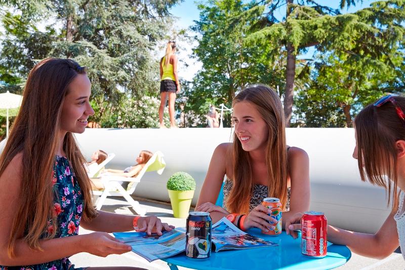 3 ados buvant des sodas avec un magazine pendant une pause dehors lors du séjour linguistique