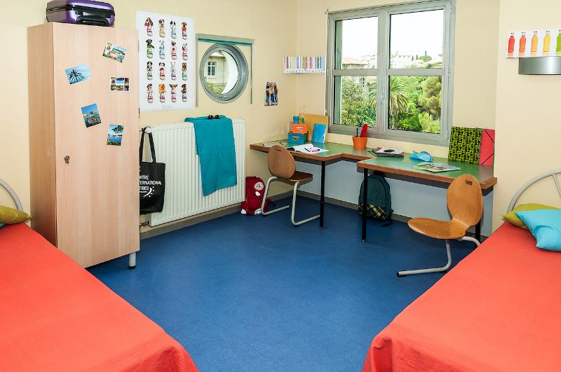 Chambre du séjour linguistique avec deux lits, deux bureaux avec des chaises et une petite armoire