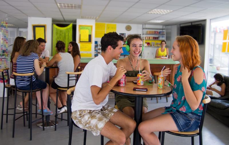 Jeunes à une table de la cafétéria du séjour linguistique avec des sodas en train de rigoler