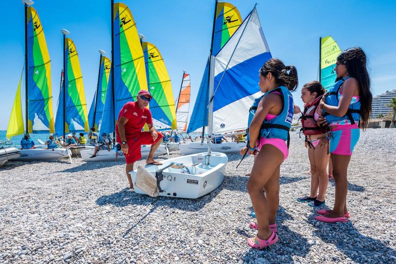 filles sur la plage avec un professeur et des bateaux sur le sable pour un cours de voile pendant le séjour linguistique
