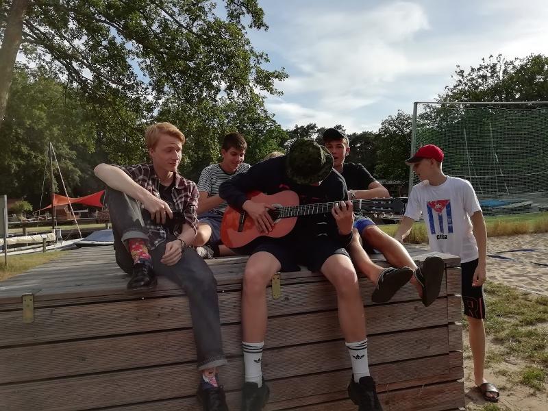 Groupe de garçon dehors avec un d'entre eux qui joue de la guitare pendant le sejour linguistique allemand