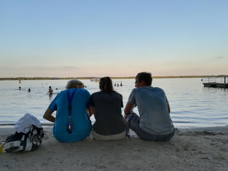 Moniteurs du sejour linguistique allemand assis sur la plage face au coucher de soleil pendant que des enfants se baignent