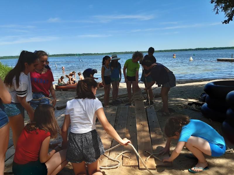 Adolescent en train d'assembler des planches avec des cordes pour construire un radeau lors de leur sejour linguistique allemand