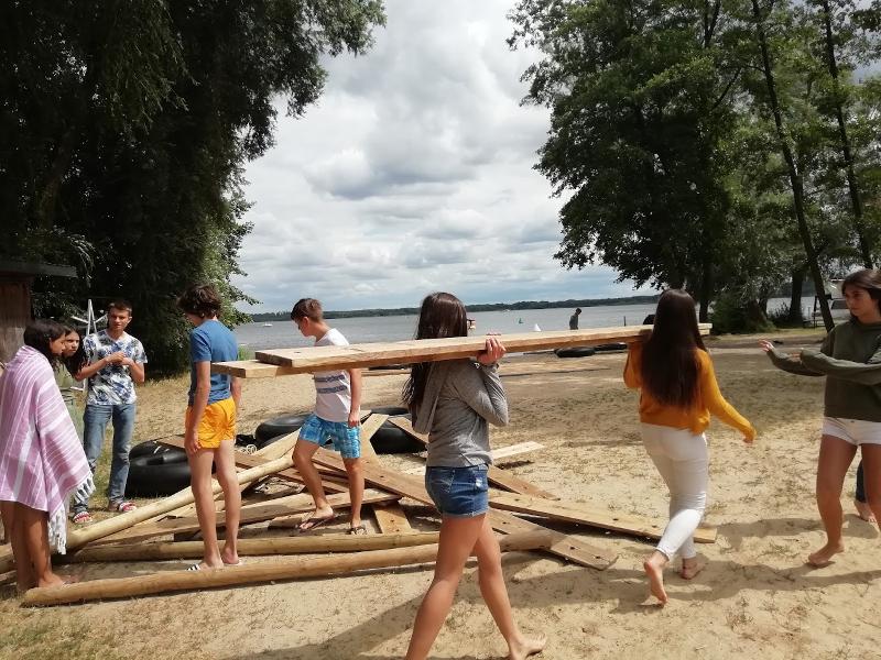 Jeunes portant du bois sur la plage pour construire un radeau lors de leur sejour linguistique allemand 