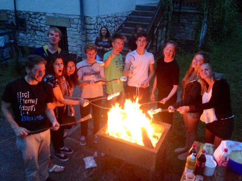 Groupe du sejour linguistique allemand en train de faire cuire su pain sur des morceaux de bois autour d'un feu de camp