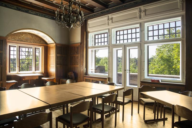 Salle de classe du sejour linguistique allemand avec des grandes tables, un lustre au plafond et des fenêtres