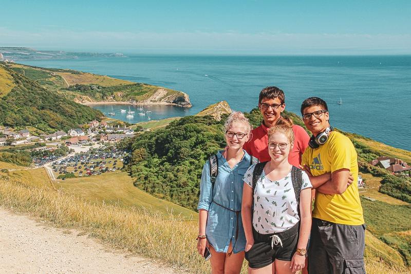 4 jeunes avec en fond un village, un petit port et la mer dans un voyage linguistique angleterre